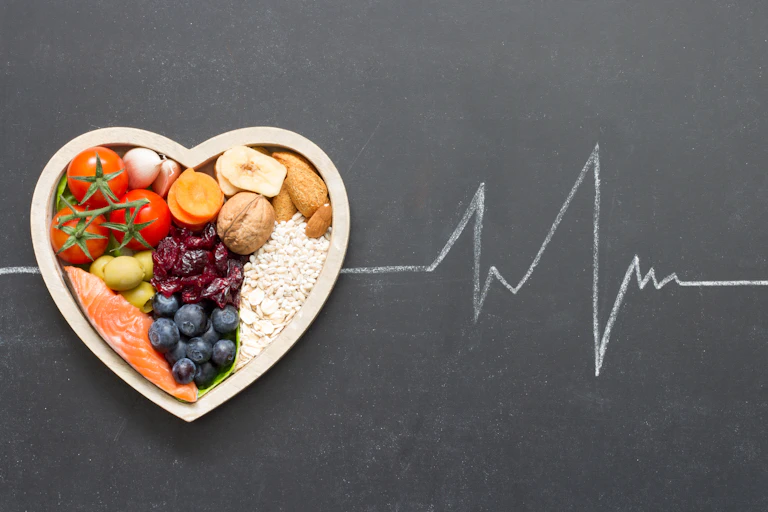 A heart-shaped dish of healthy foods against a blackboard with a chalk outline of a EKG reading