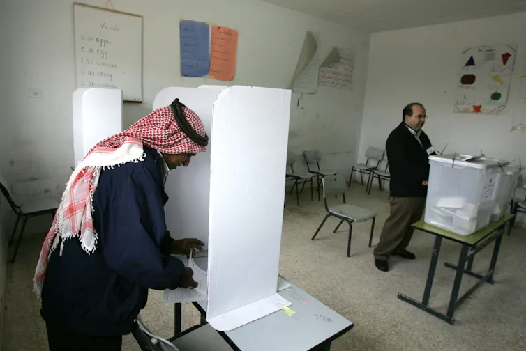 Two men stand at a voting booth in a room