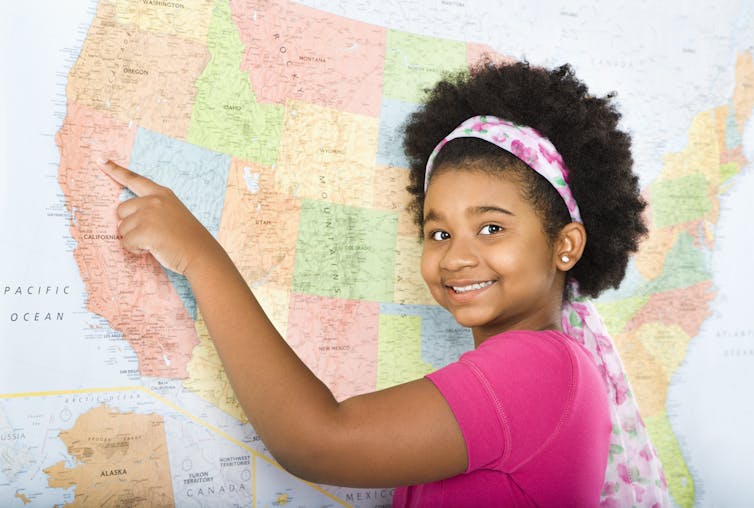 A girl points to California on a U.S. map.