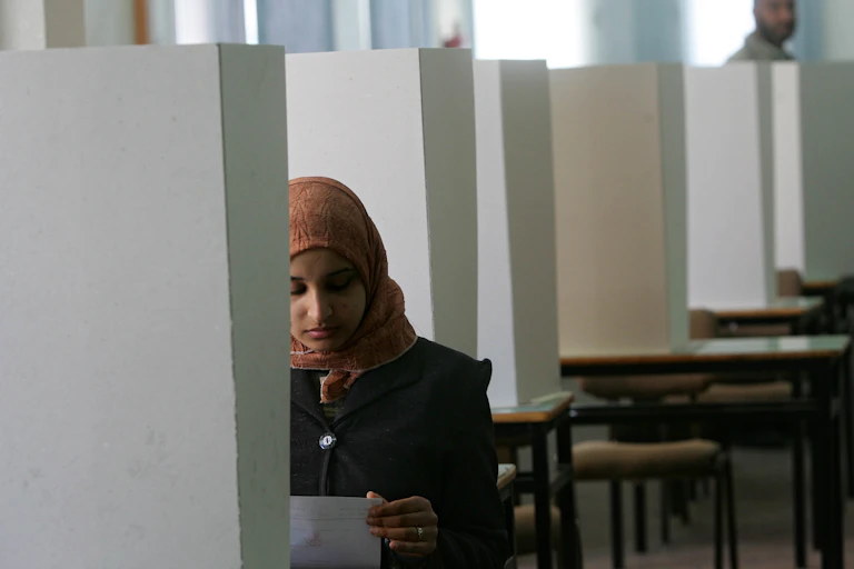 A woman in a headscarf looks at a sheet of paper in a cubicle.