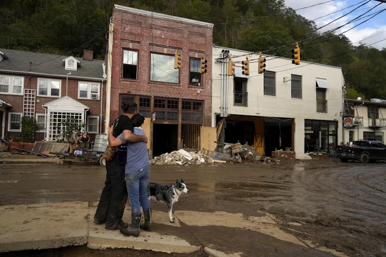 Two people hug each other in support as they look at the damaged downtown. Buildings' bottom floors were washed out by the flooding and mud is everywhere