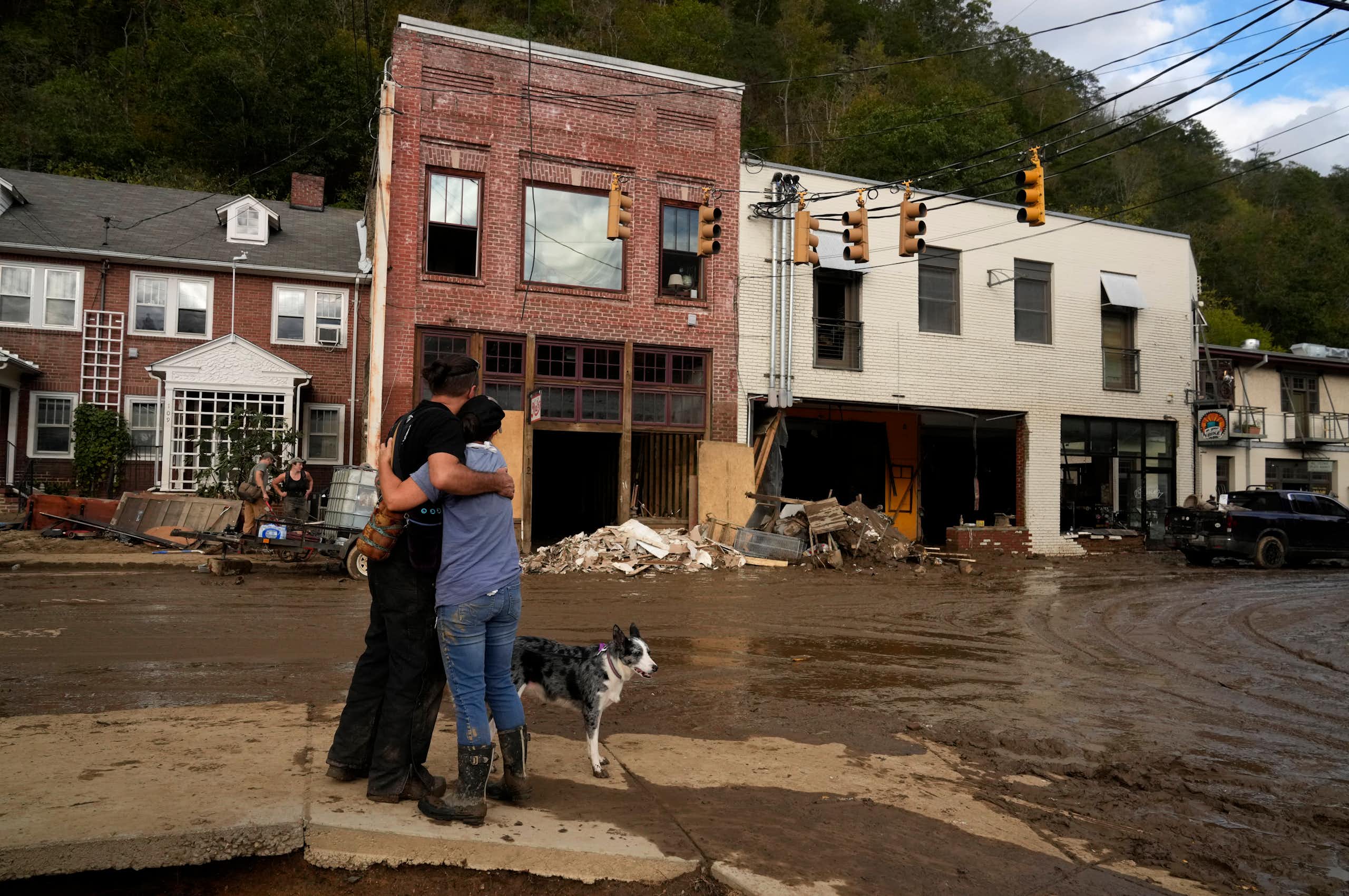 Two people hug each other in support as they look at the damaged downtown. Buildings' bottom floors were washed out by the flooding and mud is everywhere
