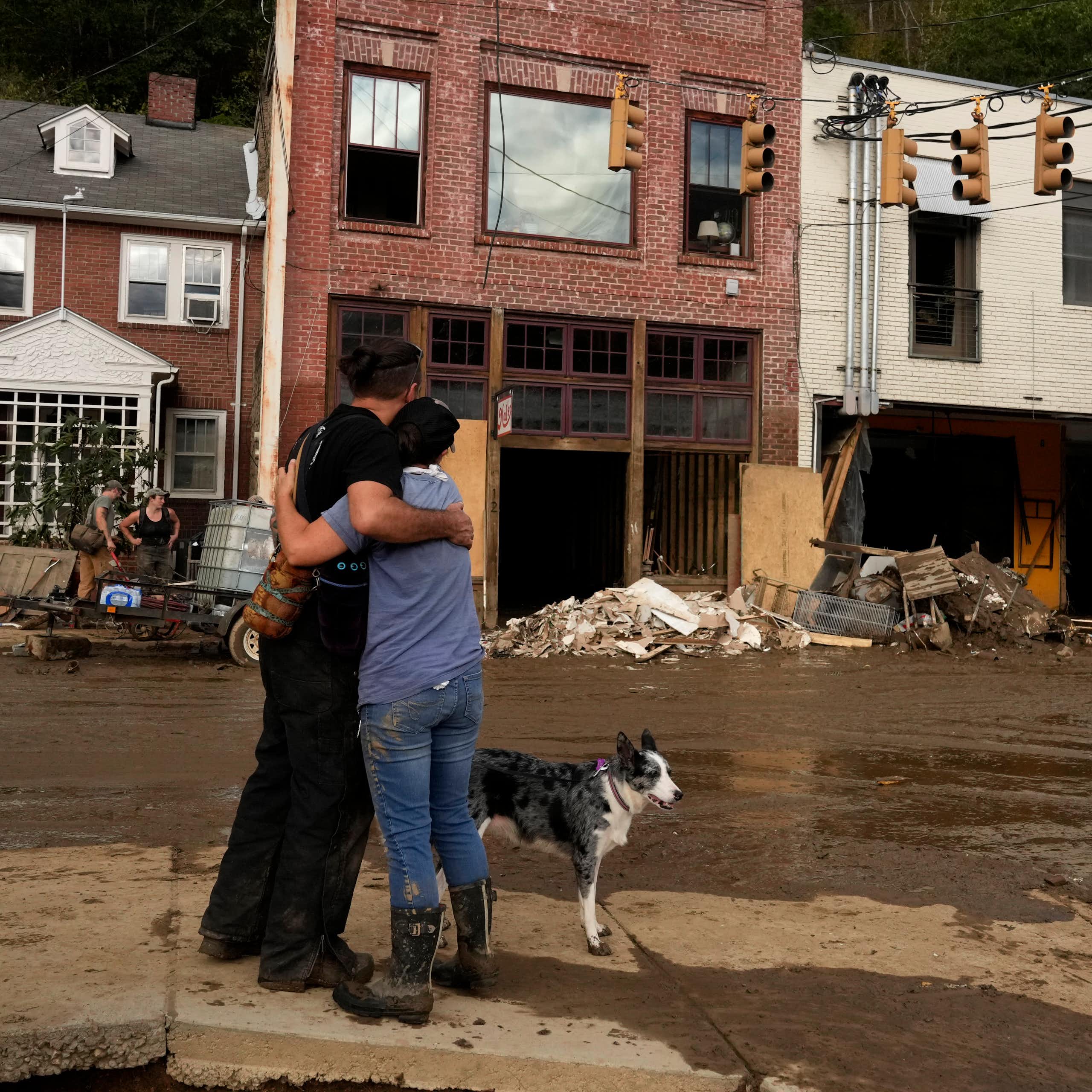 Two people hug each other in support as they look at the damaged downtown. Buildings' bottom floors were washed out by the flooding and mud is everywhere