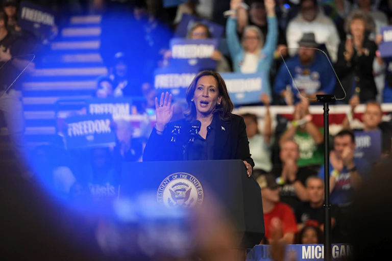 A woman speaks at a podium with a cheering crowd behind her
