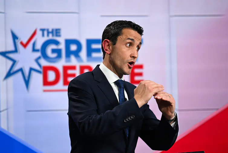A man in a suits speaks and gesticulates