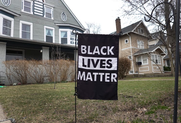 A 'Black Lives Matter' sign sits on a lawn in front of a stately house