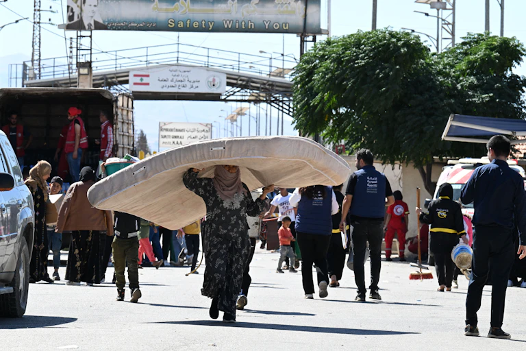 Seorang perempuan membawa kasur di kepalanya saat berjalan menyusuri jalan.