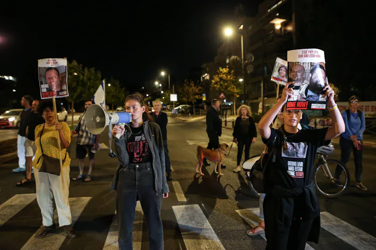 Israeli protesters demonstrate at night carrying pictures of hostages.