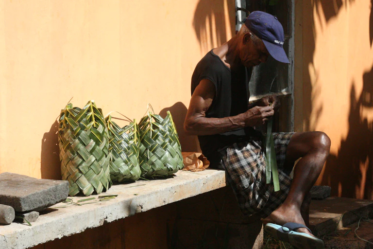 A man sitting on a bench with three woven palm baskets beside him.