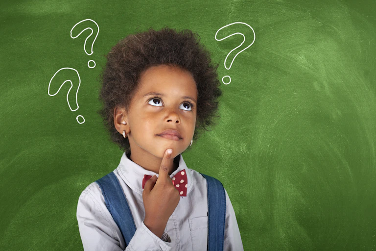 A child stands in front of a green chalkboard, one finger on their chin, comic-style question marks popping out of their head
