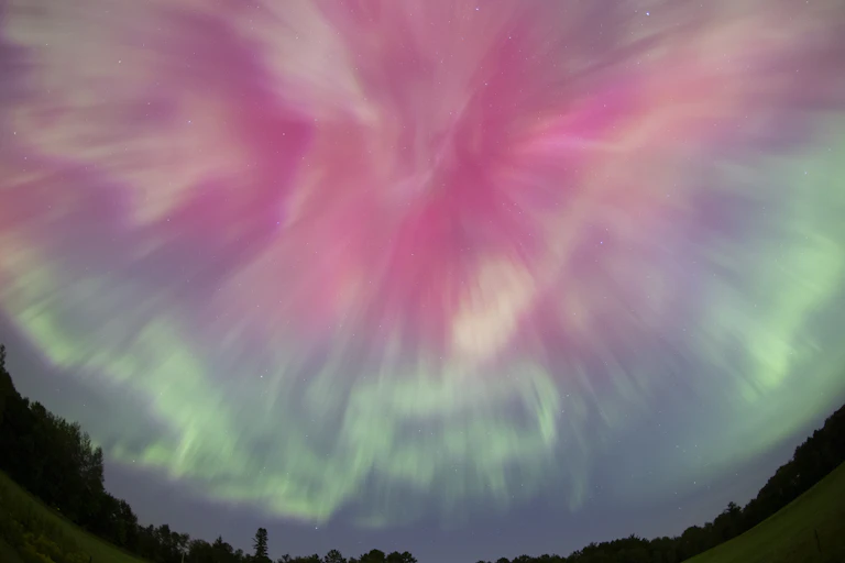 A photograph of a pink and blue eruption of light in the night sky, shot using a fish-eye lens