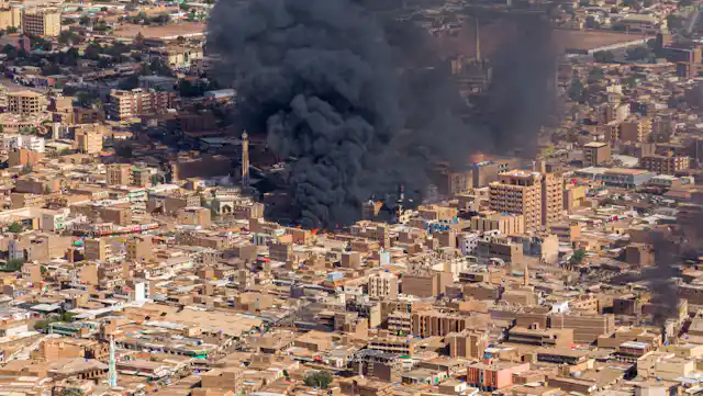 A huge cloud of black smoke rises from a city.