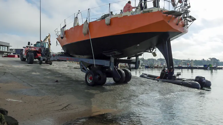 Un bateau rouge et noir, sur une remorque, est en train d’être mis à l’eau