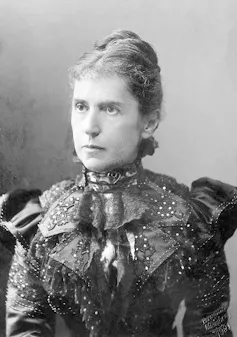 A black and white portrait of a woman in an ornate dress, with a serious expression on her face.