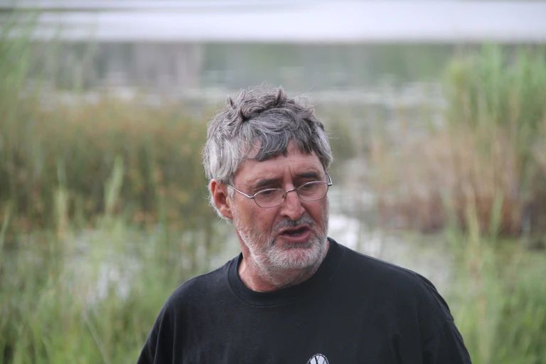 A man with greying hair and glasses speaks as his photo is taken against a backdrop of nature.