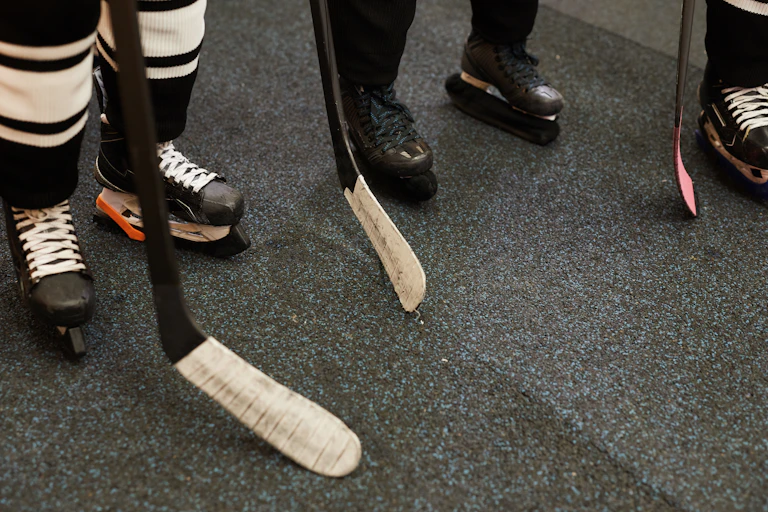 Three pairs of feet in hockey skates, with sticks.