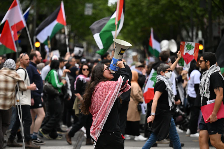 A woman yells into a megaphone against the backdrop of a large protest crowd