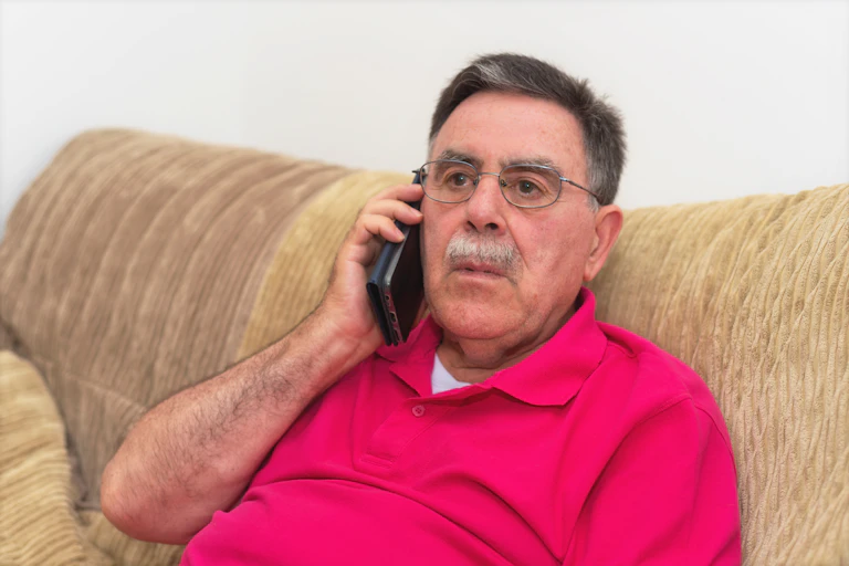 An elderly man with a worried expression speaks on the phone