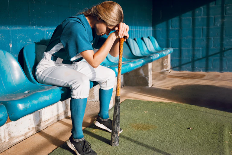 A woman baseballer sits dejectedly on the bench