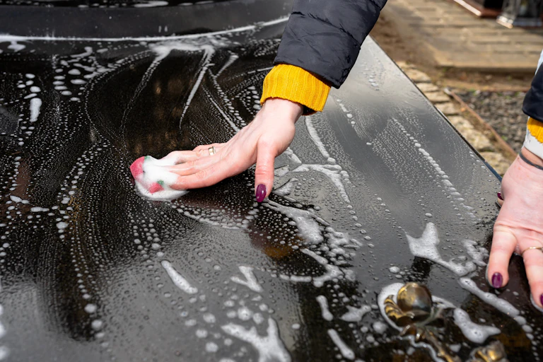 Someone washes a black grave with soap, with only their hands showing.