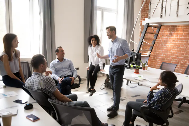 Group of people sitting in an office listening to a man who is standing