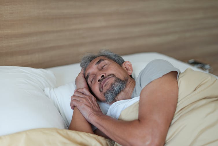An older man sleeps peacefully in bed.