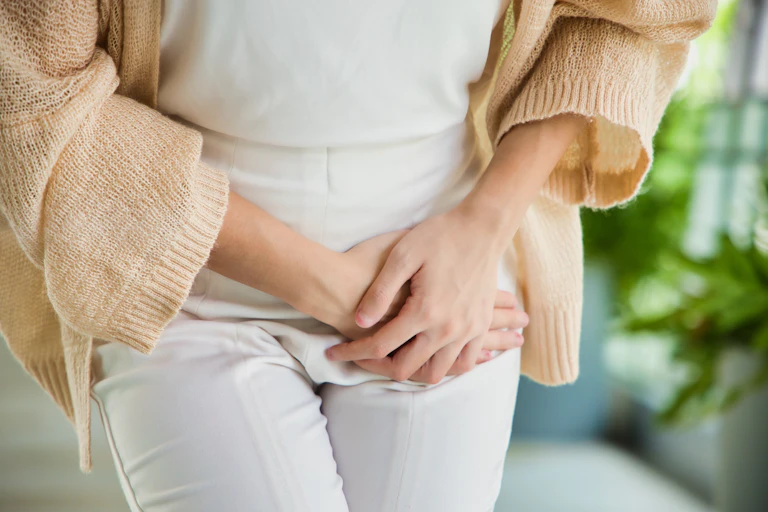A woman holding her hands over her left groin.