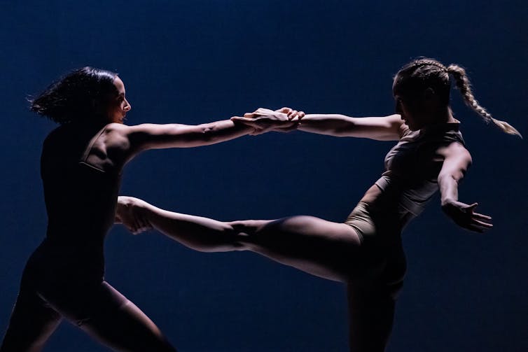 two dancers face each other on stage with arms and legs extended towards each other