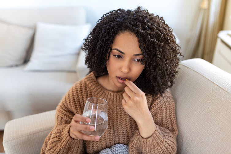A woman sitting on a couch taking a pill.
