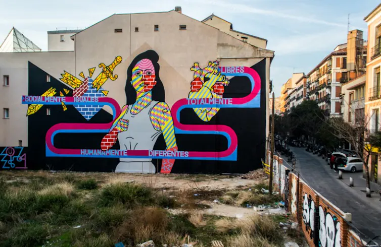 Pintura en una medianera con una figura femenina con un corazón a un lado y un puñal roto al otro.