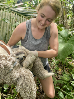 Heather (article author) woman holding sloth fitted with tracker equipment, surrounded by forest