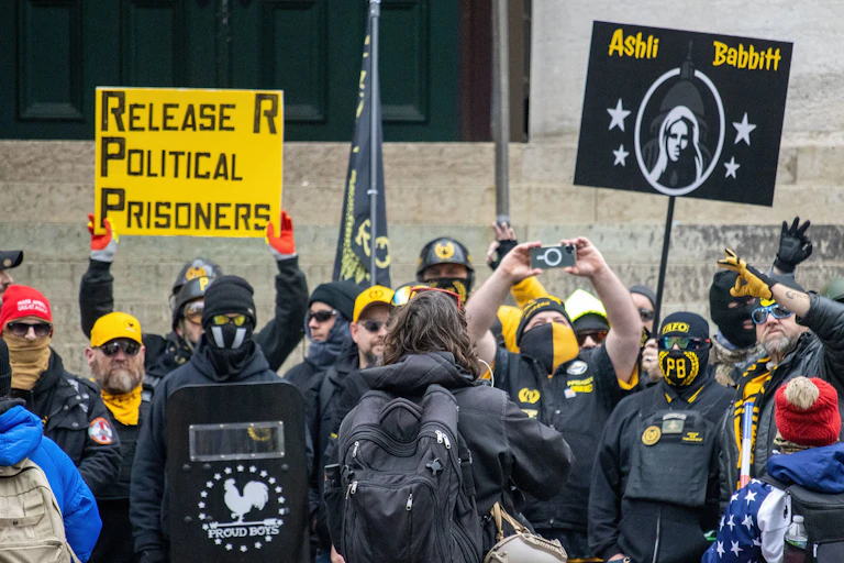 A group of white men dressed in military fatigues carry a flag that says Proud Boys.