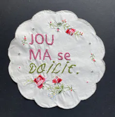 An embroidered artwork with flowers and writing on a doily and Afrikaans words