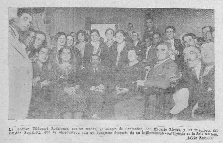 Dos mujeres y varios hombres posan para una foto en un periódico.