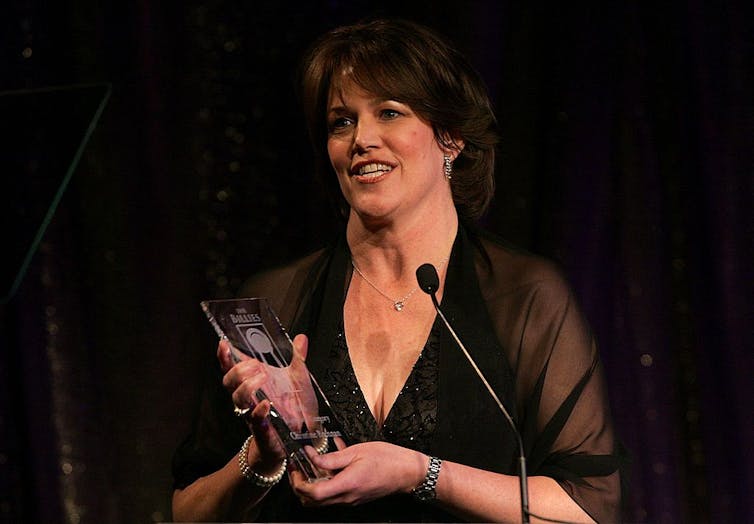 Woman speaks into microphone while holding a glass trophy.