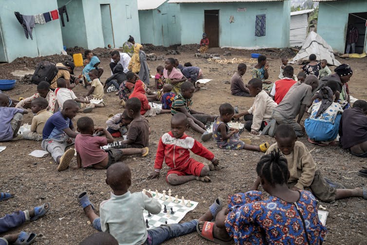 A group of young children sit on the ground playing chess