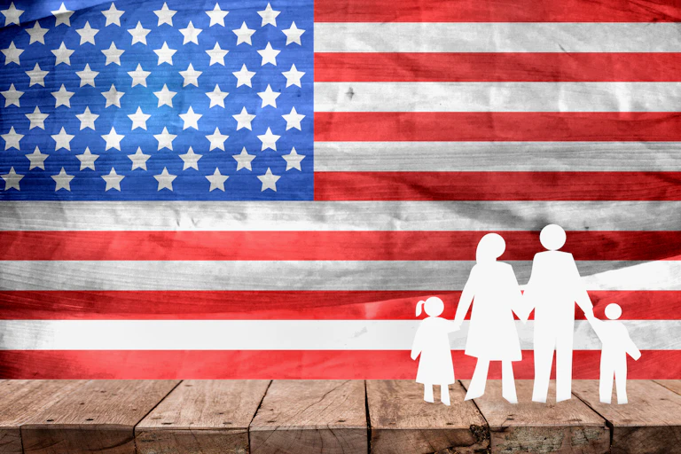 A white cutout of 2 adults holding the hands of 2 kids is seen against an American flag backdrop.