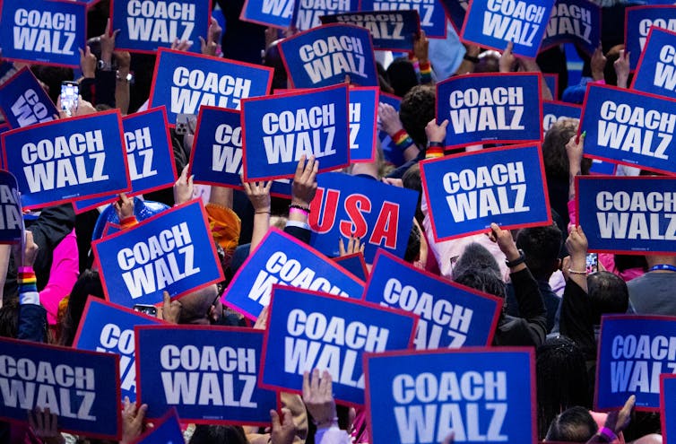 A sea of 'Coach Walz' signs in red, white and blue, held up by people in a crowd.