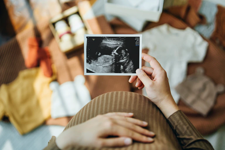 Woman looking at an ultrasound scan photo while gently touching her baby bump