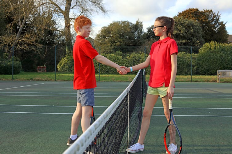 A boy and girl shake hands after a tennis match.