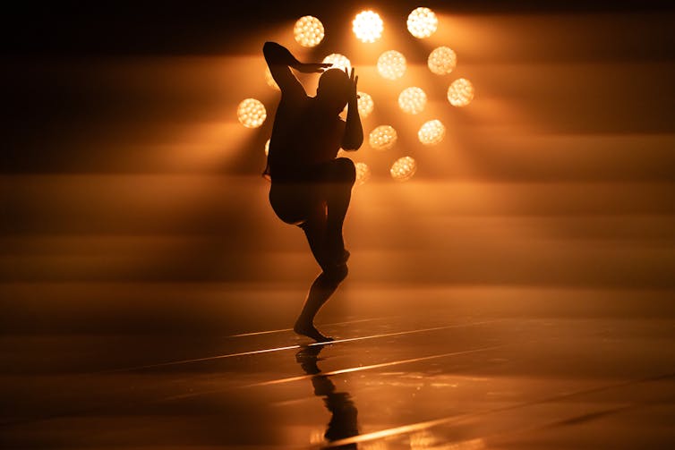 dancer on stage with orange tinted lighting behind him