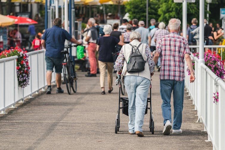 An elderly man and a woman with a walker stroll into a crowd.