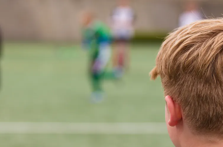 A young boy watches children on a field.