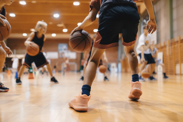 Young children bounce basketballs on an indoor court.