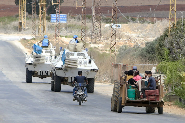 Syrian refugees ride a tractor behind Unifil armoureed cars, southern Lebanon, September 2024.