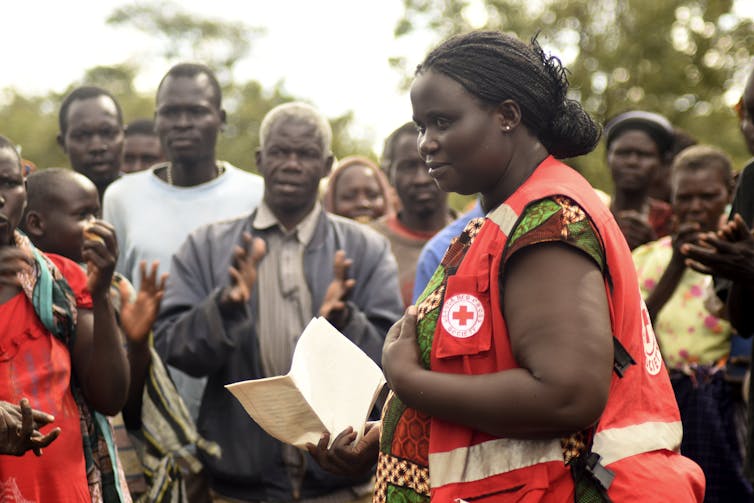 A woman in a Red Cross vest speaks with villagers.