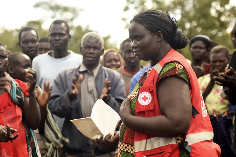 A woman in a Red Cross vest speaks with villagers.
