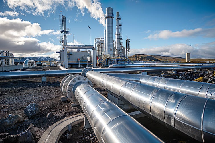 Metal pipes over Icelandic earth with a steam chimney in the distance.