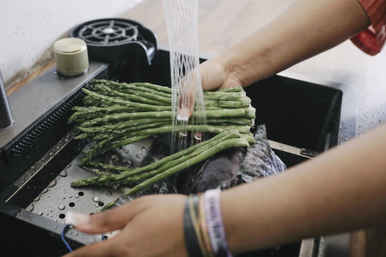 A person's hands washing asparagus in a kitchen sink