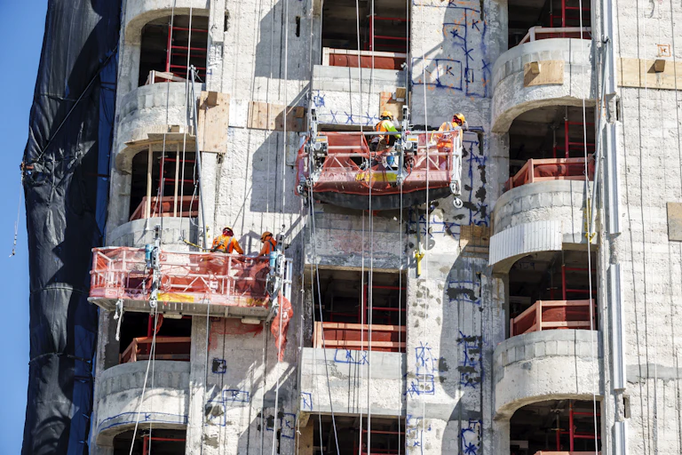 Workers on lifts work on the concrete facade of a windowless building